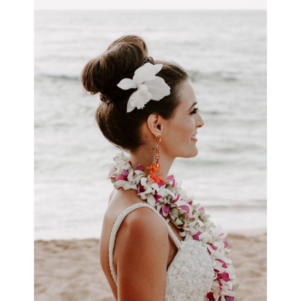 Girl on the beach wearing high-up Bun Hawaiian hairstyle with white flower in the hair
